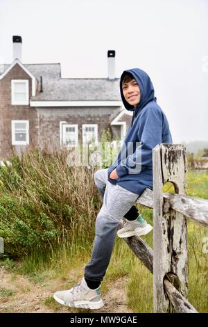Teenage boy sitting on an old wooden fence on the island of Cape Cod, Massachusettes Stock Photo