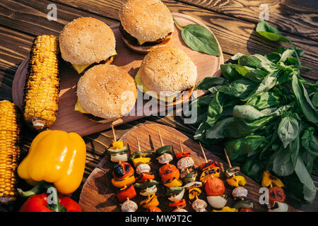 Hot delicious burgers and vegetables cooked outdoors on grill Stock Photo