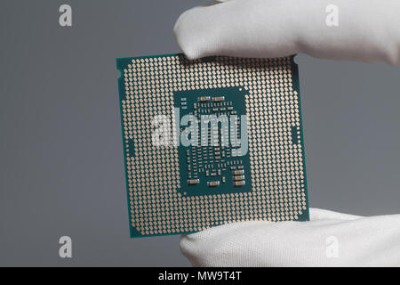 Hand in white glove holding a CPU computer processor microchip on gray Stock Photo
