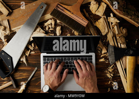 cropped image of carpenter typing on laptop surrounded by different tools on table Stock Photo