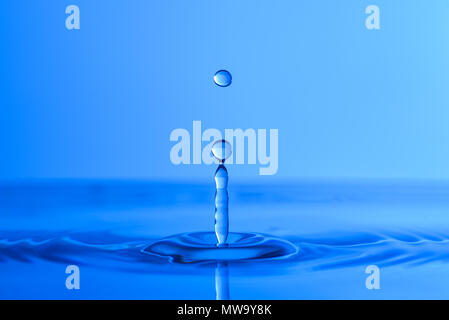 Water drop splash into crystal clear blue water making ripples background Stock Photo