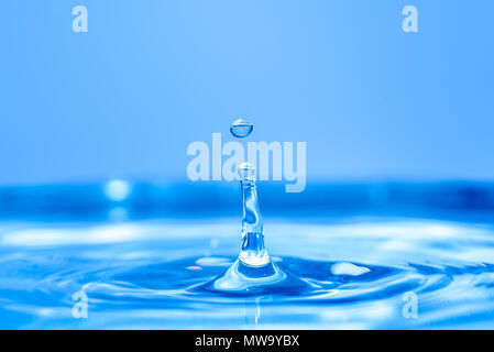 Water drop splash into crystal clear blue water making ripples