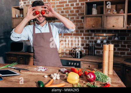 funny young man covering eyes with tomatoes while cooking Stock Photo