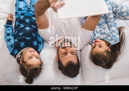 top view of happy handsome father and daughters using tablet in bed Stock Photo