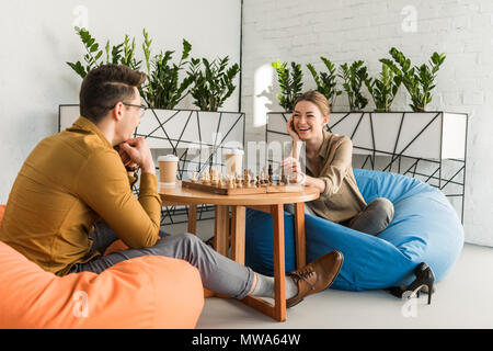 young happy friends playing chess while sitting on beanbags Stock Photo