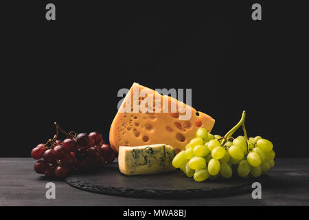 Blue cheese and emmental on board with grapes on black Stock Photo