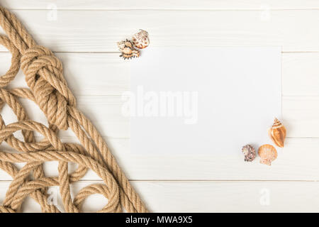 top view of brown nautical knotted rope and empty paper with seashells on white wooden surface Stock Photo