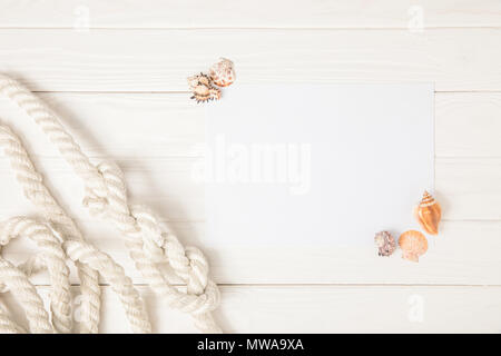 top view of white nautical knotted rope and empty paper with seashells on wooden surface Stock Photo