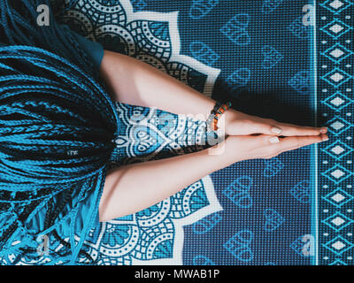Concentrated woman with blue african braids praying with wooden rosary mala beads. Namaste. Close up hands on yoga mat with mandala. Top view. Stock Photo