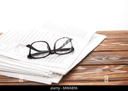 eyeglasses on pile of newspapers on wooden table, on white Stock Photo