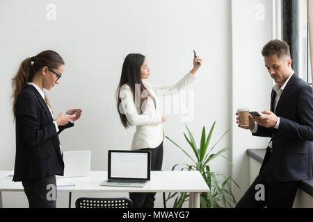 Businesspeople using smartphones texting, taking selfie in offic Stock Photo