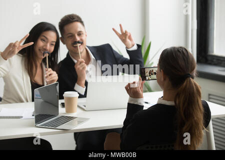 Coworker taking picture on smartphone of colleagues with fake mu Stock Photo