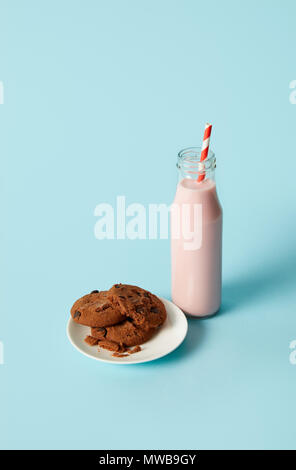 chocolate cookies in saucer and strawberry milkshake in bottle with drinking straw on blue background Stock Photo