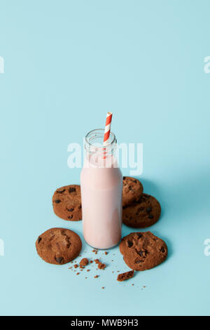 strawberry milkshake in bottle with drinking straw surrounded by chocolate cookies on blue background Stock Photo