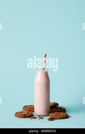 closeup view of strawberry milkshake in bottle with drinking straw surrounded by chocolate cookies on blue background Stock Photo