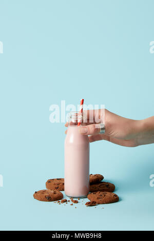 cropped image of woman holding bottle with strawberry milkshake and chocolate cookies on blue background Stock Photo