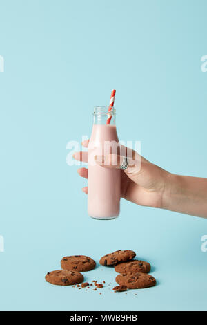 cropped shot of woman holding strawberry milkshake in bottle with drinking straw and chocolate cookies on blue background Stock Photo