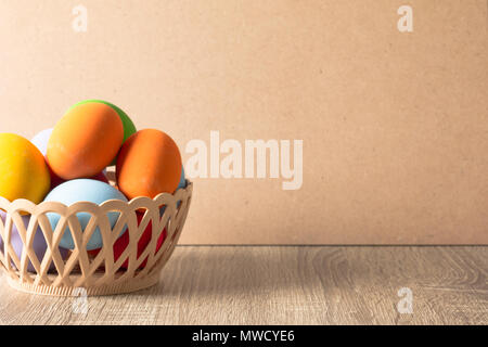 Colorful eggs are placed in a basket on a wooden table and have a brown background with copy space Stock Photo