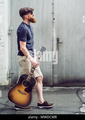 Photo of a bearded man walking with an acoustic guitar. Stock Photo