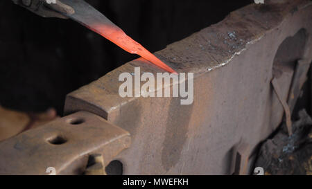 Blacksmith working metal with hammer on the anvil in the forge. hammer forging hot iron at anvil. Blacksmiths make machete. Hands of the smith by the work. Philippines. Stock Photo
