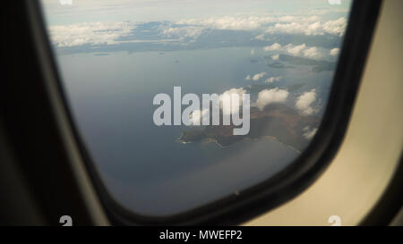 View through an airplane window on the tropical island, ocean, sea, sky and clouds. Aerial view sea, clouds and sky as seen through window of an aircraft. Travel concept. Stock Photo