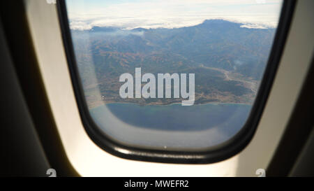 View through an airplane window on the tropical island, ocean, sky and clouds. Aerial view sea, clouds and sky as seen through window of an aircraft. Travel concept. Stock Photo