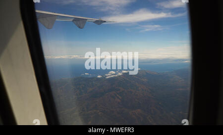 View through an airplane window on the tropical island, ocean, sky and clouds. Aerial view sea, clouds and sky as seen through window of an aircraft. Travel concept. Stock Photo