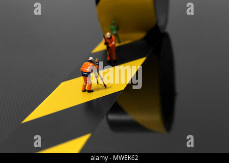 Miniature scale model construction workers using hazard tape on a carbon fibre surface Stock Photo