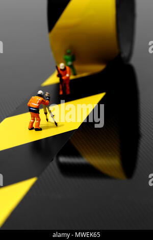 Miniature scale model construction workers using hazard tape on a carbon fibre surface Stock Photo