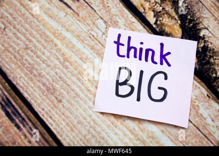Think big handwritten words on white paper with wooden bark as background. Positive messages on flat lay concept with retro background. Positive moral messages. Stock Photo