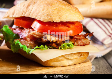 Ciabatta sandwich with smoked bacon, cheese and tomato on a cutting board Stock Photo