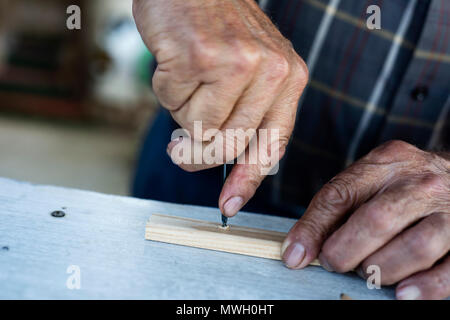 closeup of an old caucasian man making a hole in a wood strip with a gimlet Stock Photo