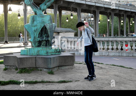 Young girl wearing beret dancing by statue with view of Pont de Bir Hakeim bridge (formerly Passy) by River Seine in Paris France Europe  KATHY DEWITT Stock Photo