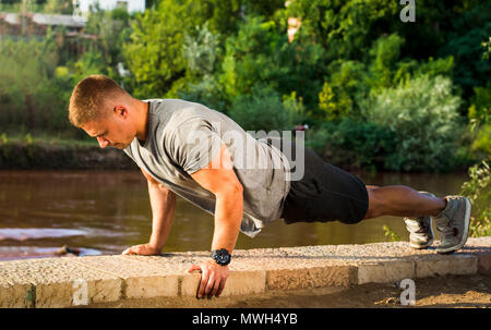 Man performing push ups by the river at sunset Stock Photo