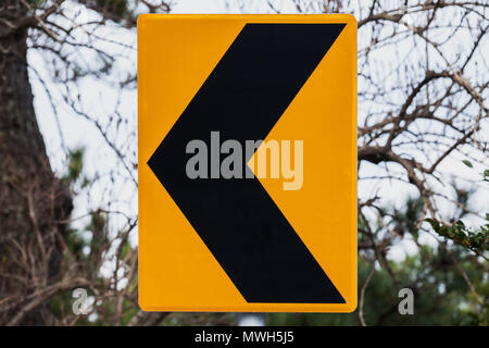 Dangerous turn left, yellow black road sign mounted on roadside Stock Photo