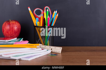 Assortment of school supplies on a wooden desktop with a blank chalkboard background for copy space Stock Photo