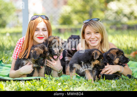 Two young smiling women lying on grass with small puppies of german shepherd Stock Photo