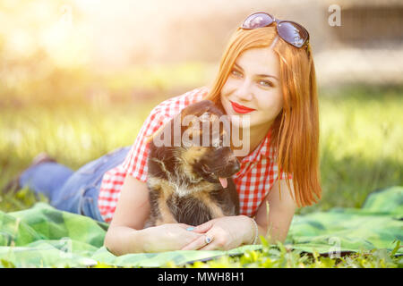 Young smiling woman lying on grass with small puppy of german shepherd Stock Photo