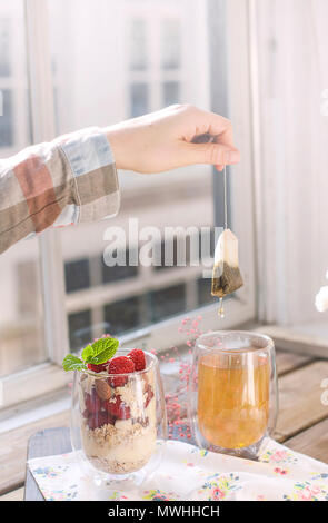 Tea in a glass and muesli, for breakfast on the table near the window, flowers and morning light. Copy space Stock Photo