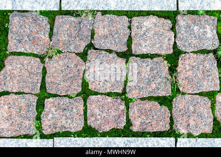 Close-up texture, background of sett blocks different texture. Vintage, Rusty tiled, colorful, decorative granite pavement with green grass and moss. Stock Photo