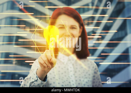 Smiling woman touching digital screen interface with her finger. Press a golden light bulb. Creativity and idea concept in the modern virtual technolo Stock Photo