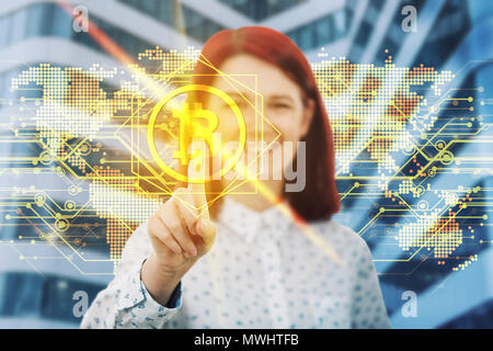 Smiling woman touching digital screen interface. Press on the golden bitcoin icon over world map hologram background. Modern technology, virtual crypt Stock Photo