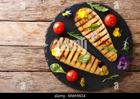 Portion of grilled eggplant and tomato with herbs and edible flowers close-up on the table. horizontal top view from above Stock Photo