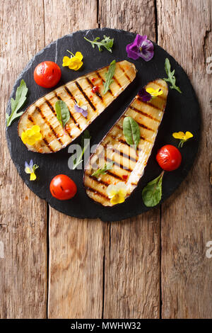 Portion of grilled eggplant and tomato with herbs and edible flowers close-up on the table. Vertical top view from above Stock Photo