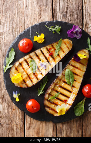 Organic food: grilled eggplant and tomatoes with herbs and edible flowers close-up on the table. Vertical top view from above Stock Photo