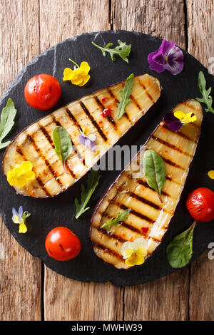 Summer appetizer from grilled eggplants and tomatoes with herbs and edible flowers close-up on the table. Vertical top view from above Stock Photo