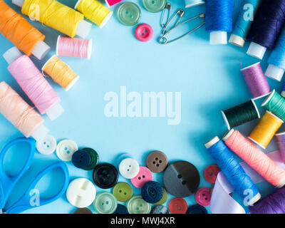Multicolored sewing threads and buttons on blue background with copy space flat lay. Stock Photo