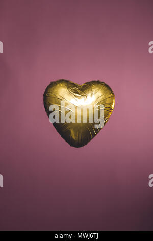 heart shaped candy in golden wrapper isolated on pink Stock Photo