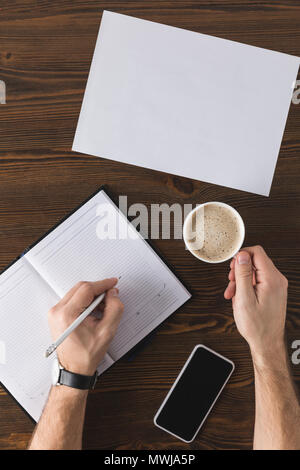 partial view of businessman making notes in notebook at table Stock Photo