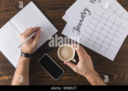 partial view of businessman making notes in notebook at table with calendar Stock Photo